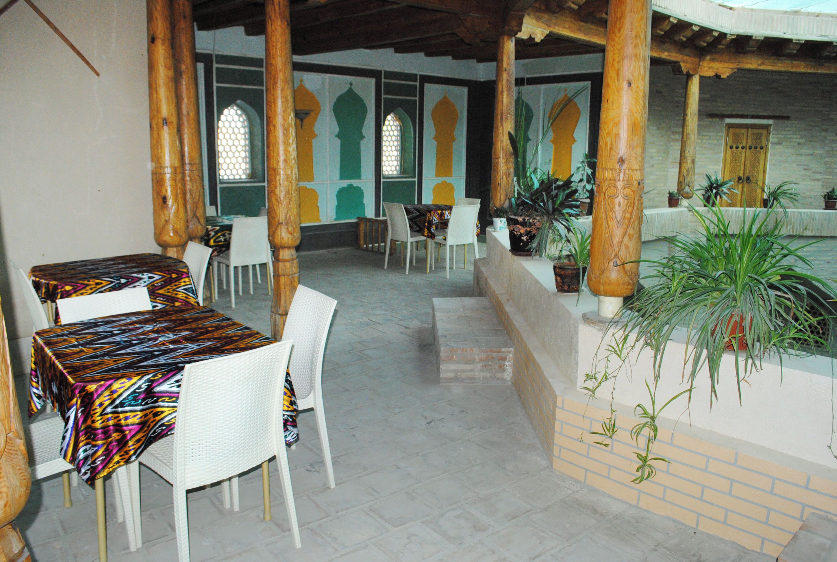 Un espace extérieur abrité, aménagé avec des tables et des chaises, des piliers en bois et des plantes en pot.