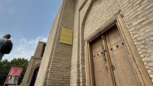 A stone building with a large wooden door and a sign on the wall. - AIST HOTEL (Bukhara)
