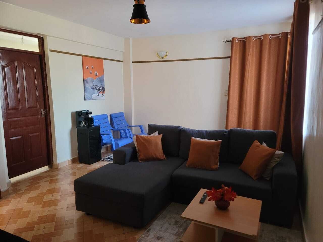 Een woonkamer met een hoekbank, een salontafel, een blauwe stoel en een deur.