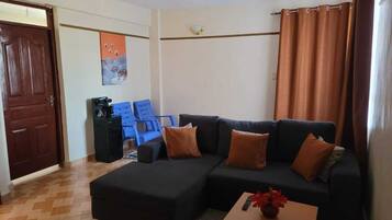 Een woonkamer met een hoekbank, een salontafel, een blauwe stoel en een deur.