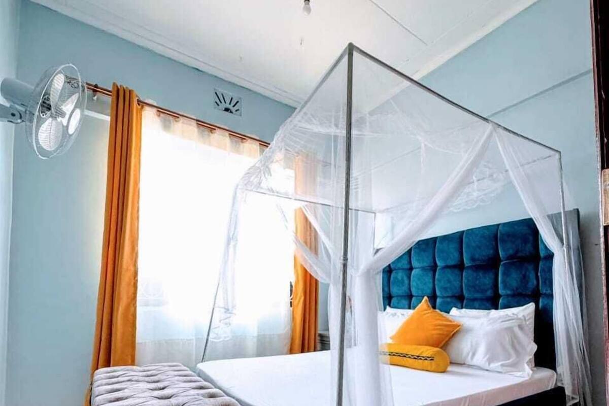 Une chambre à coucher avec un lit sous un baldaquin, une table de chevet et une fenêtre avec des rideaux.