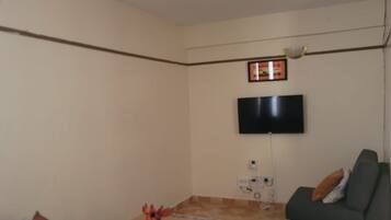 A living room with a grey sofa, a small table with a toy, a flat-screen TV mounted on the wall, and a pendant light.