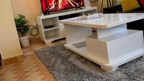 Un salon doté d’un téléviseur à écran plat, d’une table basse blanche et d’un tapis gris.