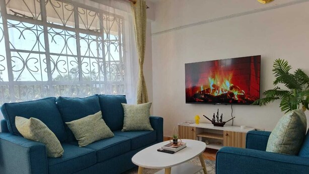 Un salon avec un canapé bleu, une table basse blanche et un téléviseur à écran plat fixé au mur.