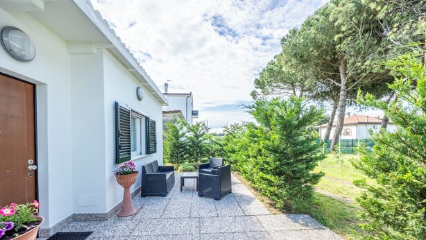 Une maison à l’extérieur blanc, avec une porte marron et un petit patio aménagé avec des meubles d’extérieur et des plantes en pot.
