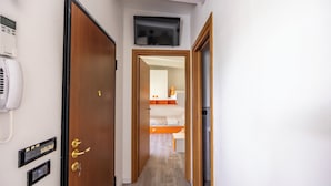 Un couloir d’hôtel avec une porte en bois, un téléphone, un panneau de commande et un lit dans la chambre adjacente.