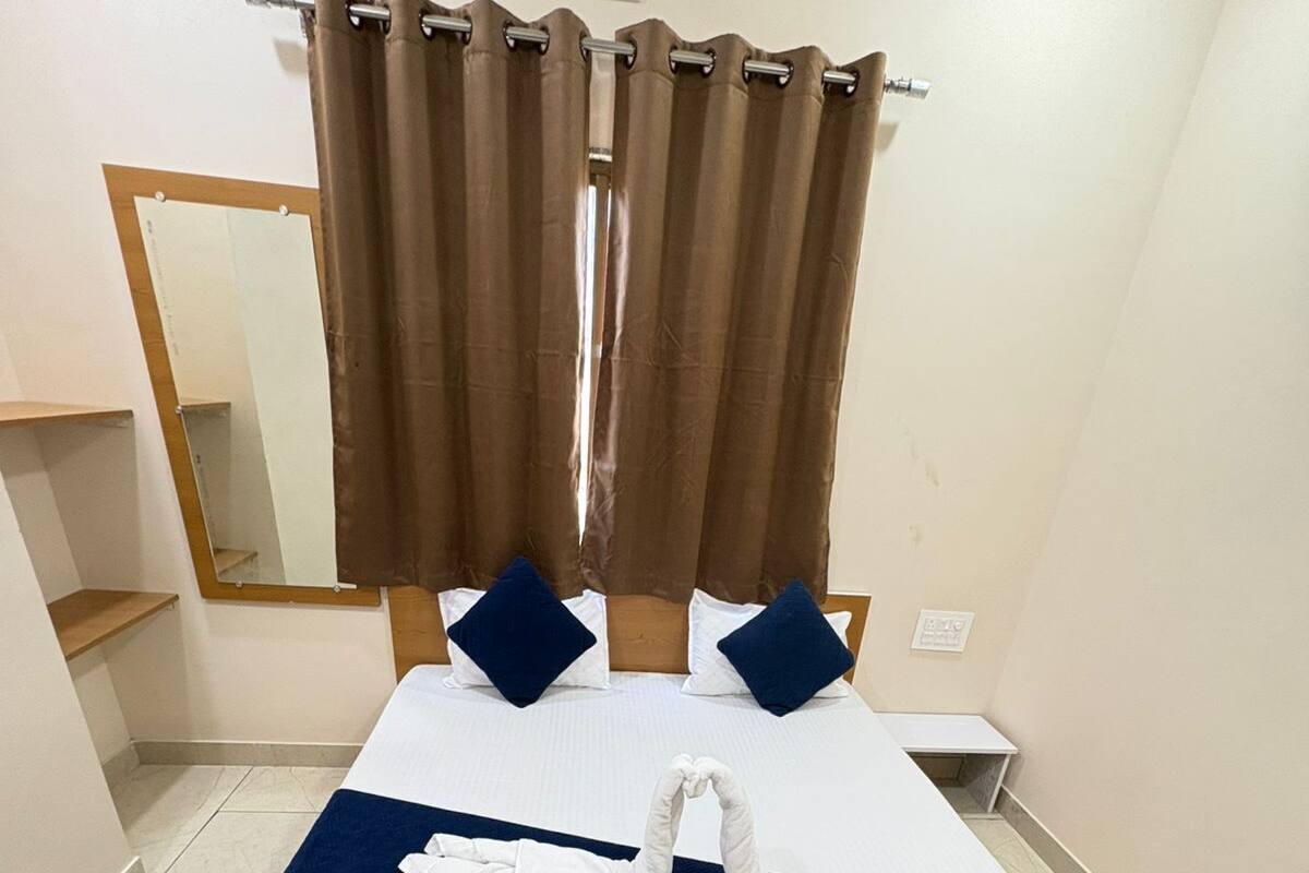 A neatly made bed with white and navy bedding, a pair of towels, and a mirror on the wall.