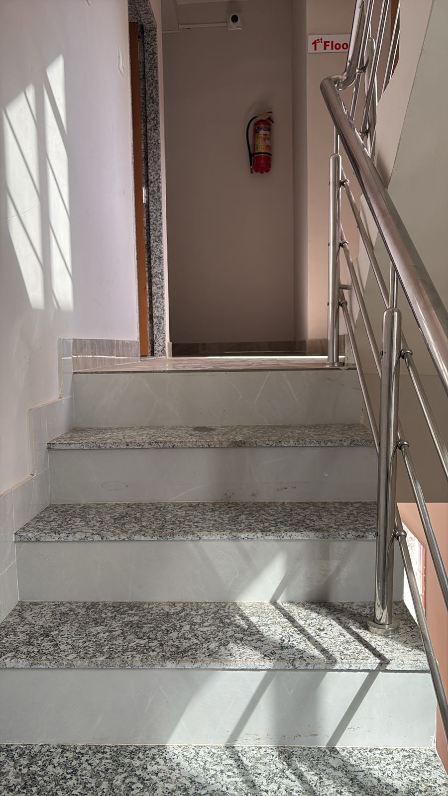 Una escalera con escalones de granito y barandillas metálicas que conduce a una habitación con un extintor en la pared.