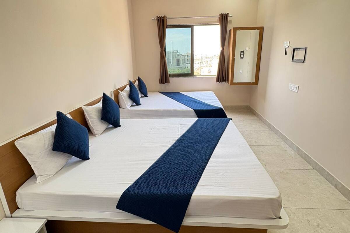 A hotel room with two beds, a ceiling fan, a window with curtains, and a city view.