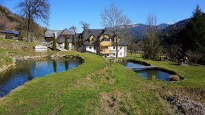 A large house with a pond and a small bridge, surrounded by trees and hills. - Apartment in St. Georgen Near Kreischbergbahn (Sankt Georgen am Kreischberg)