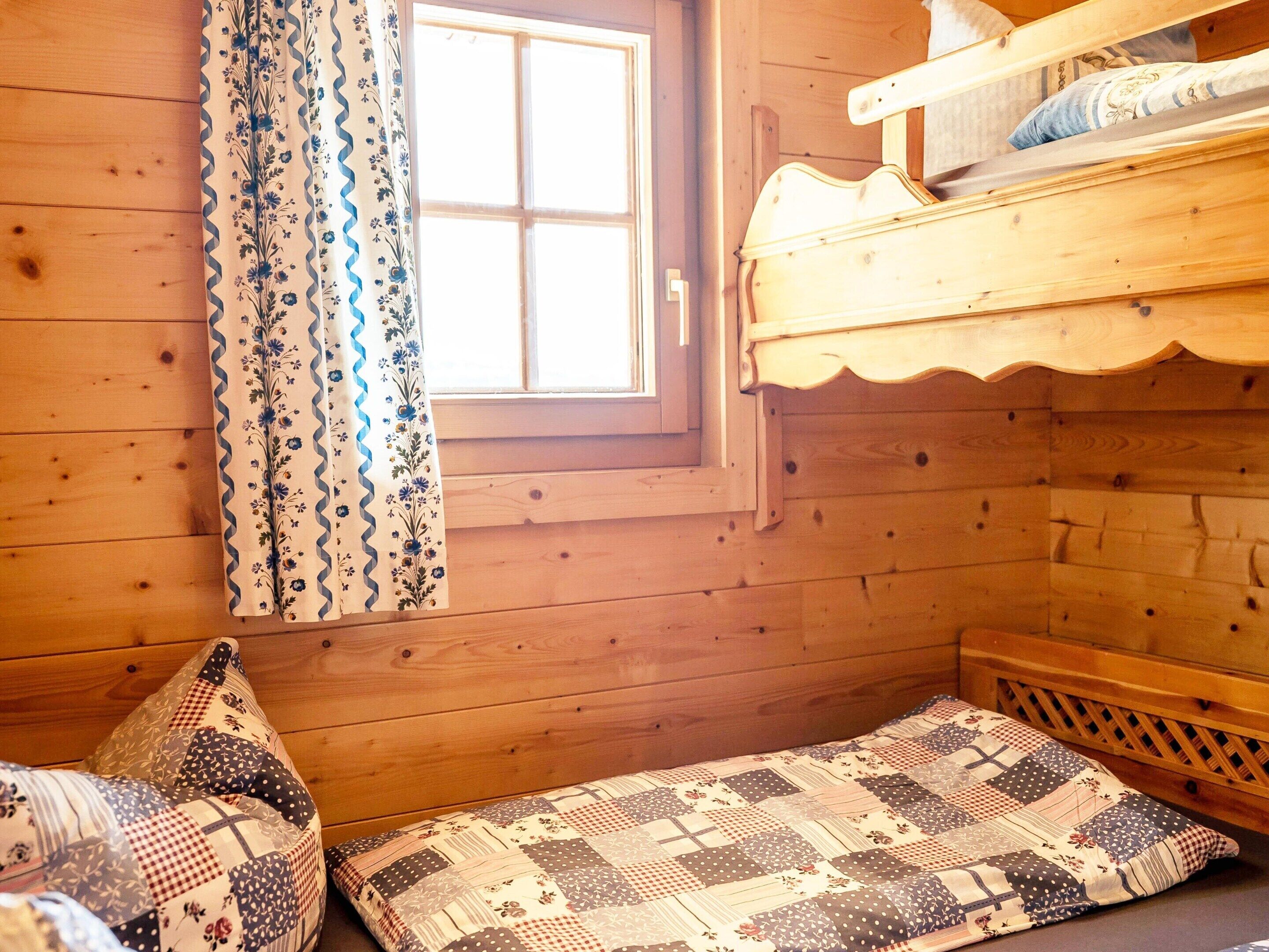 A wooden cabin room with a bunk bed, a window with curtains, and a quilted bedspread.