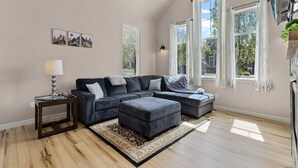 A modern living room with a sectional sofa, a small side table, and a large window with curtains.