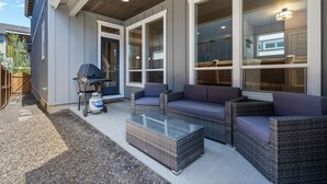 An outdoor patio with wicker furniture, a grill, and a glass table.