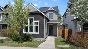 A modern two-story house with a grey exterior and white trim, a front yard with a pathway, and a wooden fence.