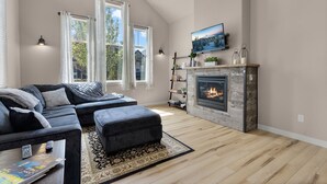 A modern living room with a sectional sofa, ottoman, fireplace, and large windows.