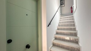 Eine Treppe mit weiß-schwarzem Hundepunktmuster, eine grüne Tür mit schwarzen Griffen und ein Feuerlöscher an der Wand.