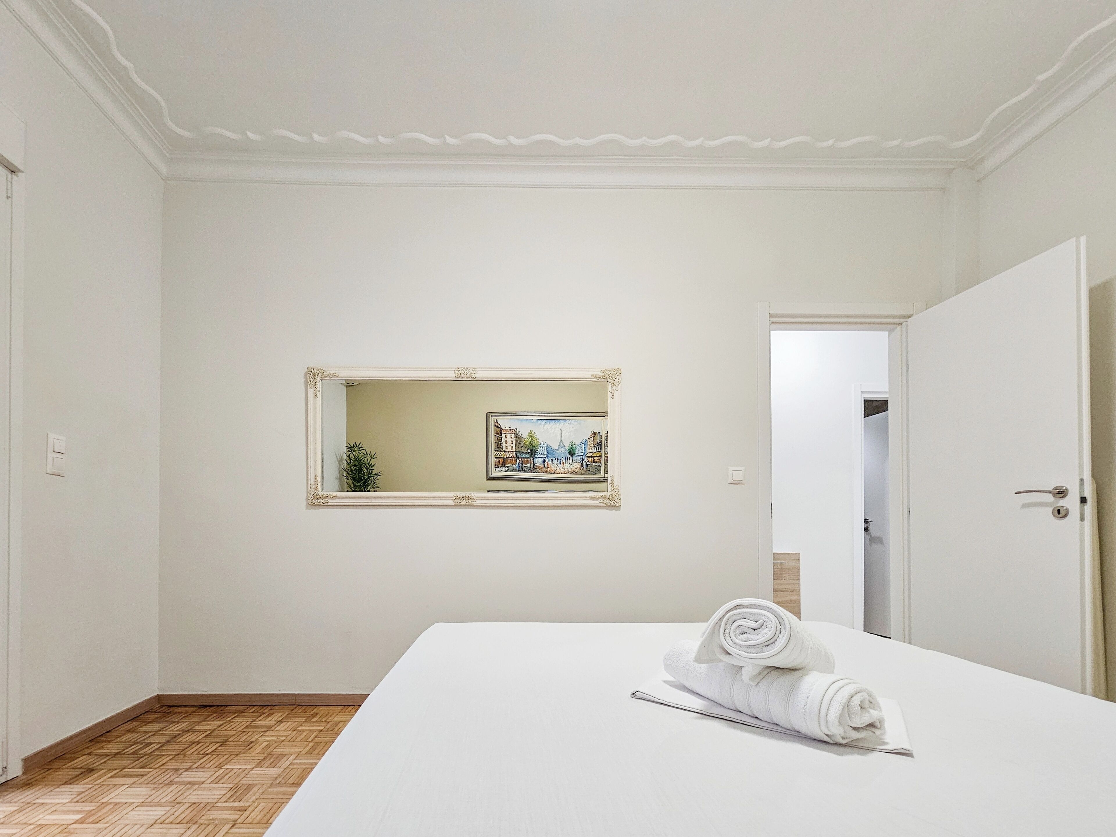 A hotel room with a large bed, a painting on the wall, and a door leading to another room.