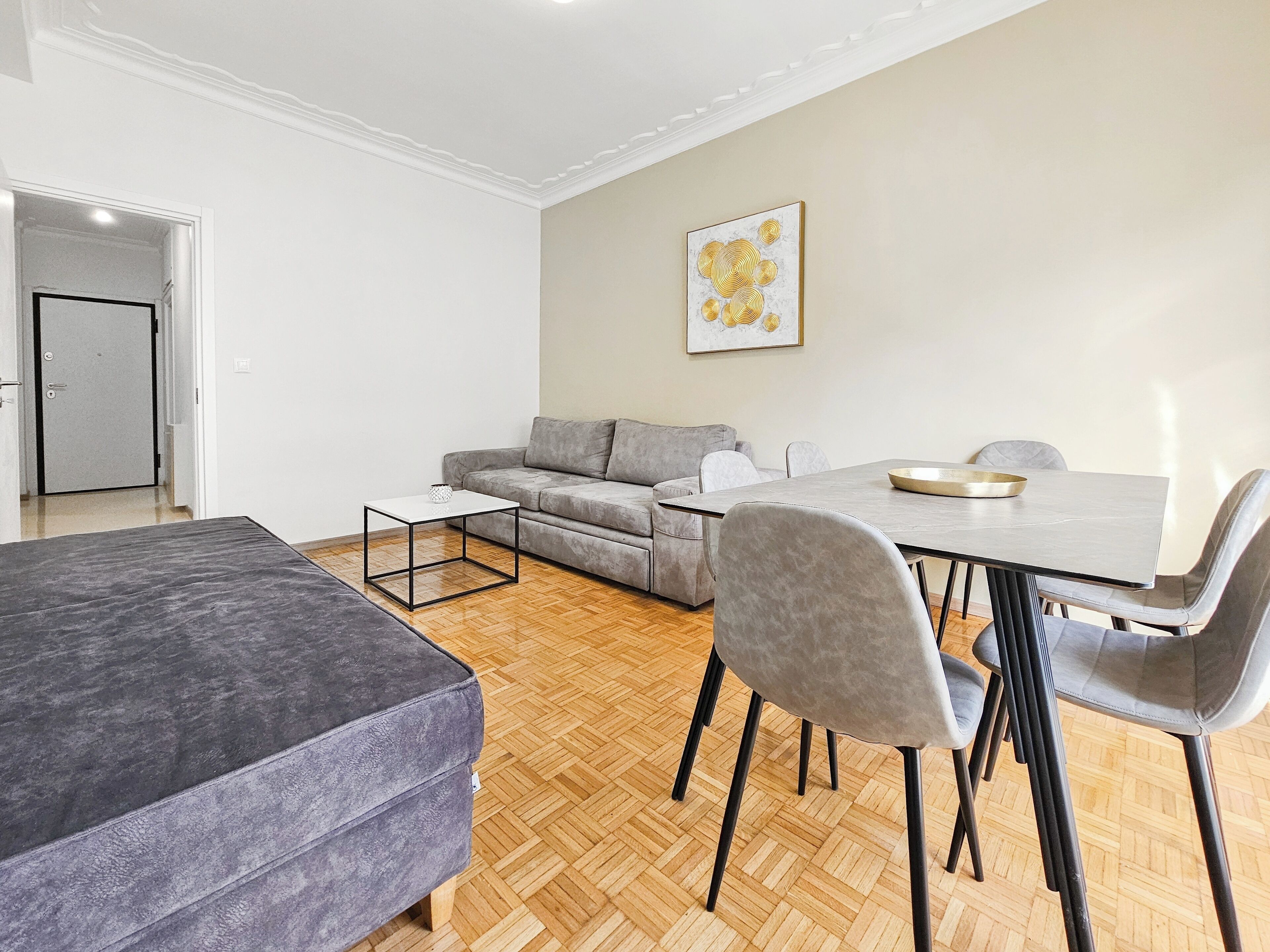 A modern living room with a grey sofa, a dining table with chairs, and a small white table.