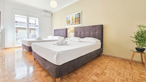 Habitación de hotel con una cama grande, una cama más pequeña, una planta en maceta y un balcón con vistas.