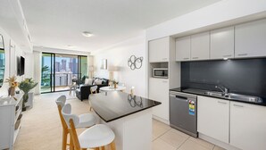 A modern kitchen with white cabinets, a black countertop, and stainless steel appliances. There is a dining area with a round table and white chairs. - Stunning unit-perfect location (Gold Coast)