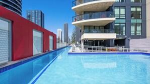 A modern hotel with a swimming pool, large windows, and a red building facade. - Stunning unit-perfect location (Gold Coast)