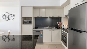 A modern kitchen with a black countertop, stainless steel appliances, and white cabinetry. - Stunning unit-perfect location (Gold Coast)
