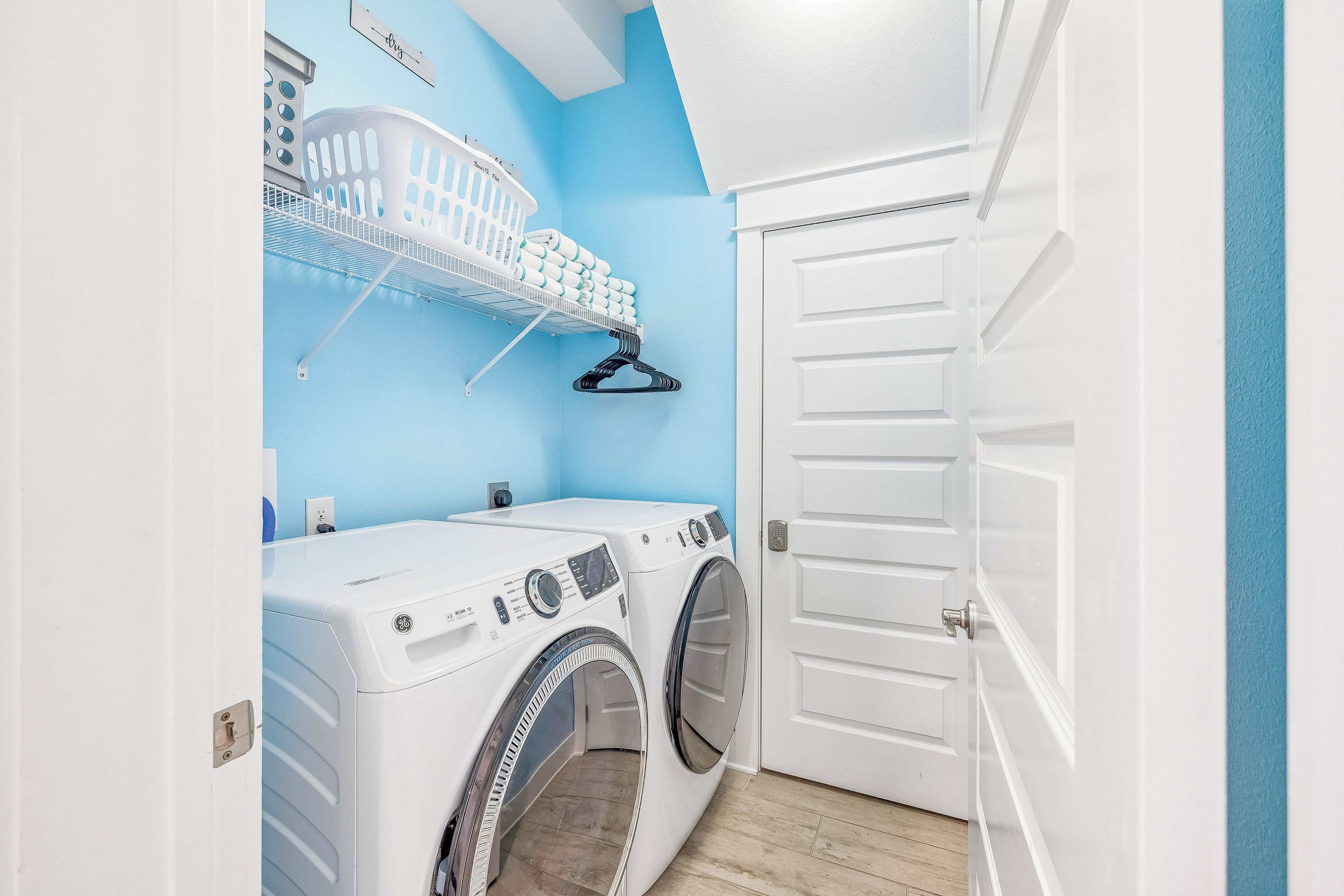 A laundry room with two front-loading washing machines, a drying rack, and a door with a handle.