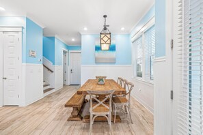 A dining area with a wooden table and chairs, a chandelier, and a staircase leading to another room.