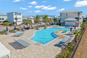 A swimming pool with lounge chairs and a paved deck, surrounded by palm trees and buildings.