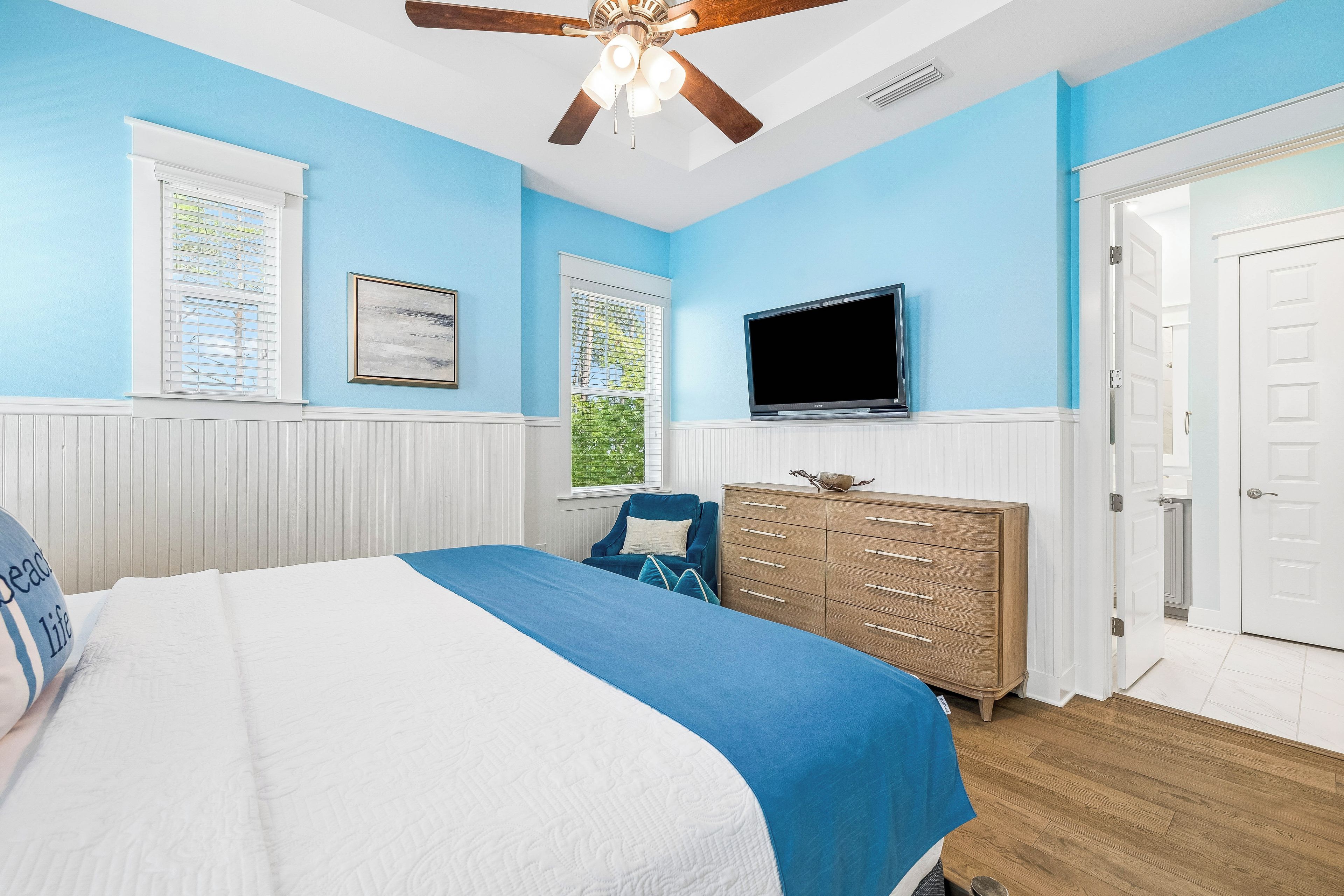 A bedroom with a bed, dresser, TV, and windows.
