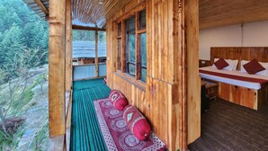 Eine Holzhütte mit einem Bett, einer Bank mit Kissen und Blick auf den Wald.
