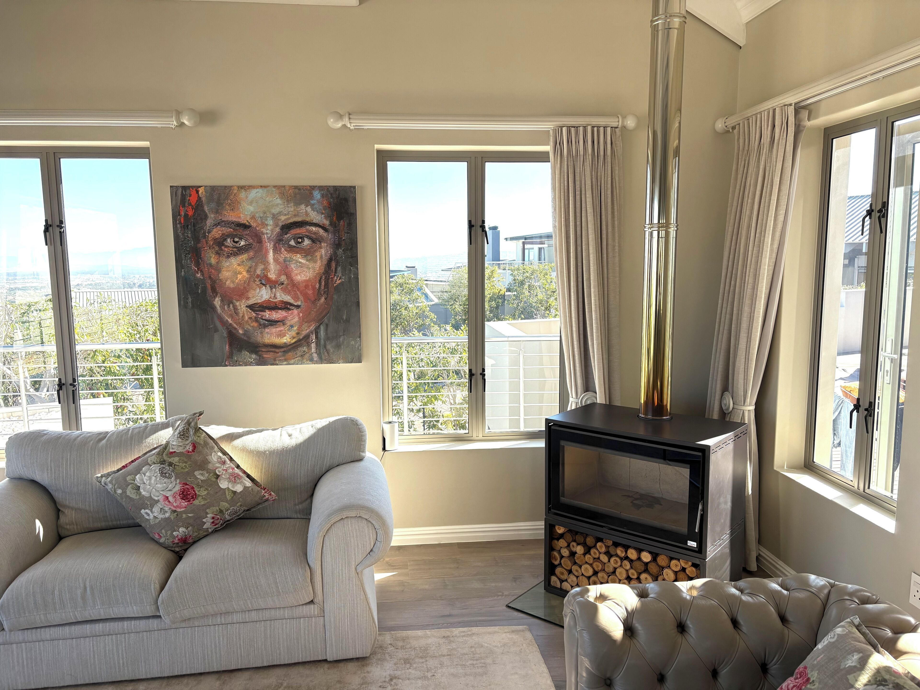 A living room with a sofa, a fireplace, a large window, and a painting on the wall.