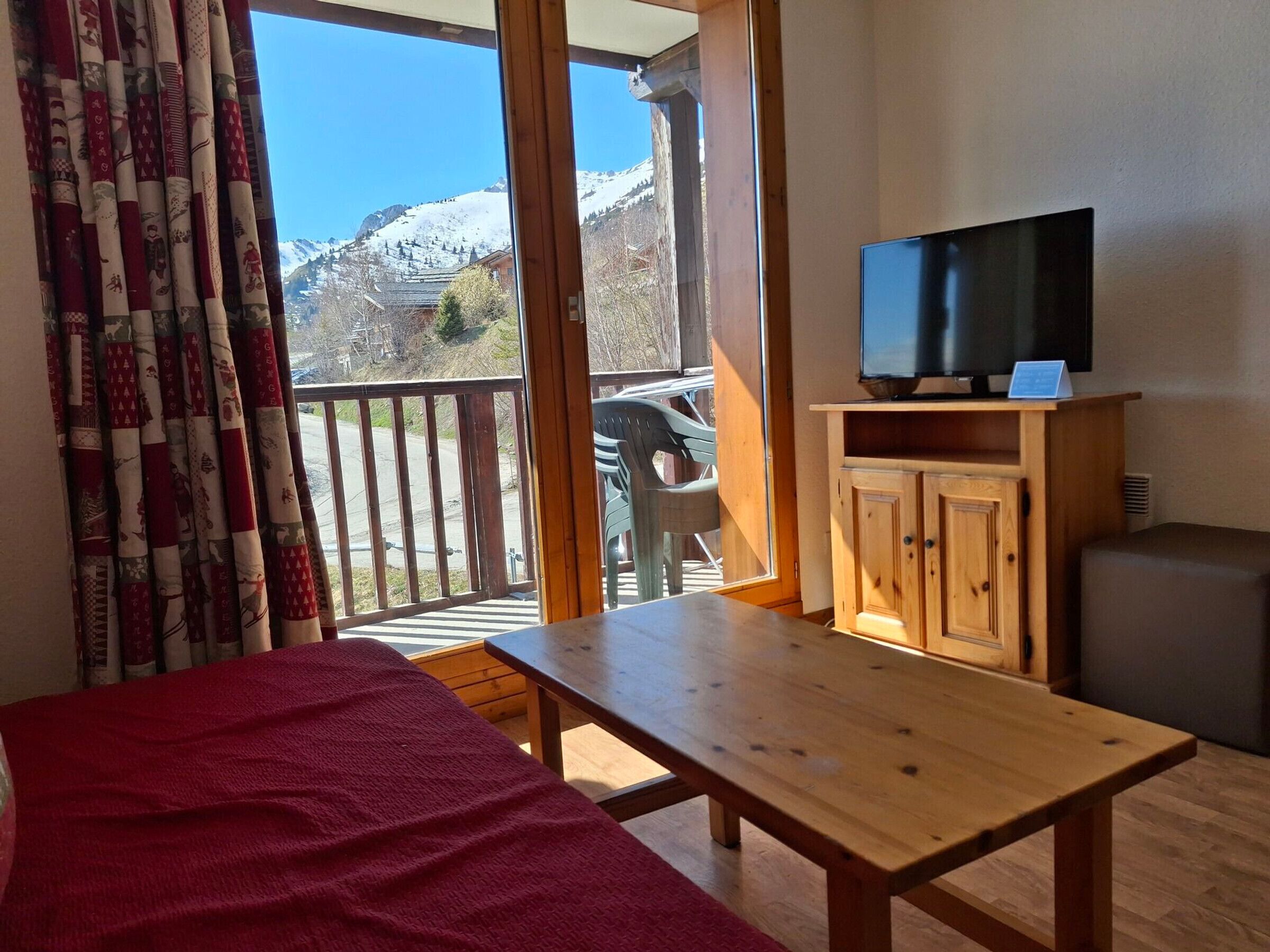 Una habitación con una cama, una mesa de madera, un televisor sobre un mueble de madera y vistas a una montaña nevada a través de un ventanal corredero.