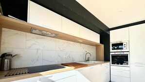 Une cuisine moderne avec des meubles blancs, un pare-feu en marbre, un plan de travail en bois et des appareils électroménagers intégrés.