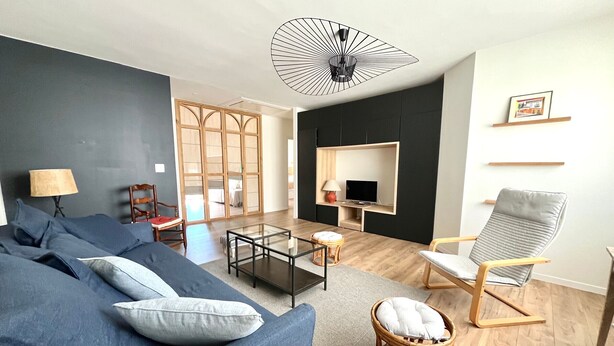 Un salon moderne avec un canapé bleu foncé, une table basse en verre, un fauteuil gris et un téléviseur fixé à un mur noir.