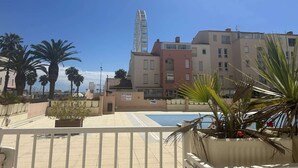 A pool area with a Ferris wheel in the background, surrounded by palm trees and multi-story buildings. - 2-Room Apartment - Port Center - Cap d'Agde (Cap d'Agde)