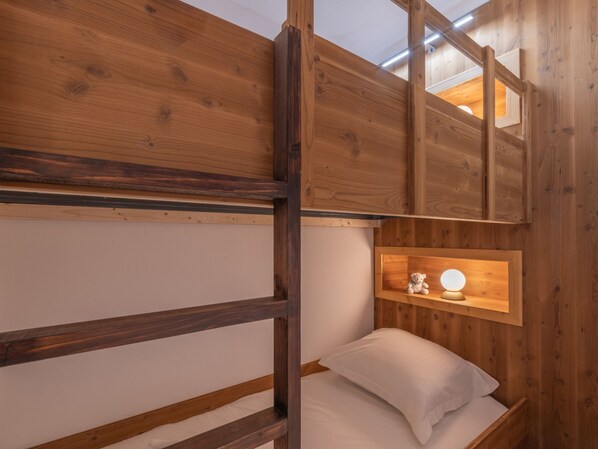 A bunk bed with a wooden headboard, a bedside table with a lamp, and a small shelf with a teddy bear.
