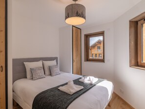 Ett sovrum med en säng, kuddar, ett täcke, en hängande lampa och ett fönster med utsikt över en byggnad.