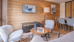 Una sala de estar moderna con una pared de madera, una chimenea, una zona de comedor con mesa y sillas, y un cuadro colgado.