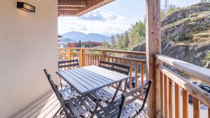 Terraza de madera con mesa y sillas, con vistas a un paisaje montañoso.