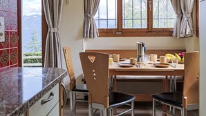 A kitchen with a wooden table, two chairs, a coffee maker, and a view of mountains through the window.