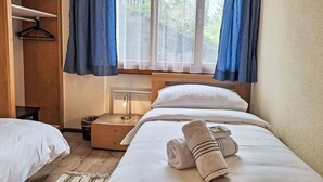 A bedroom with a bed, a bedside table, a lamp, a hanging coat rack, and a window with curtains.