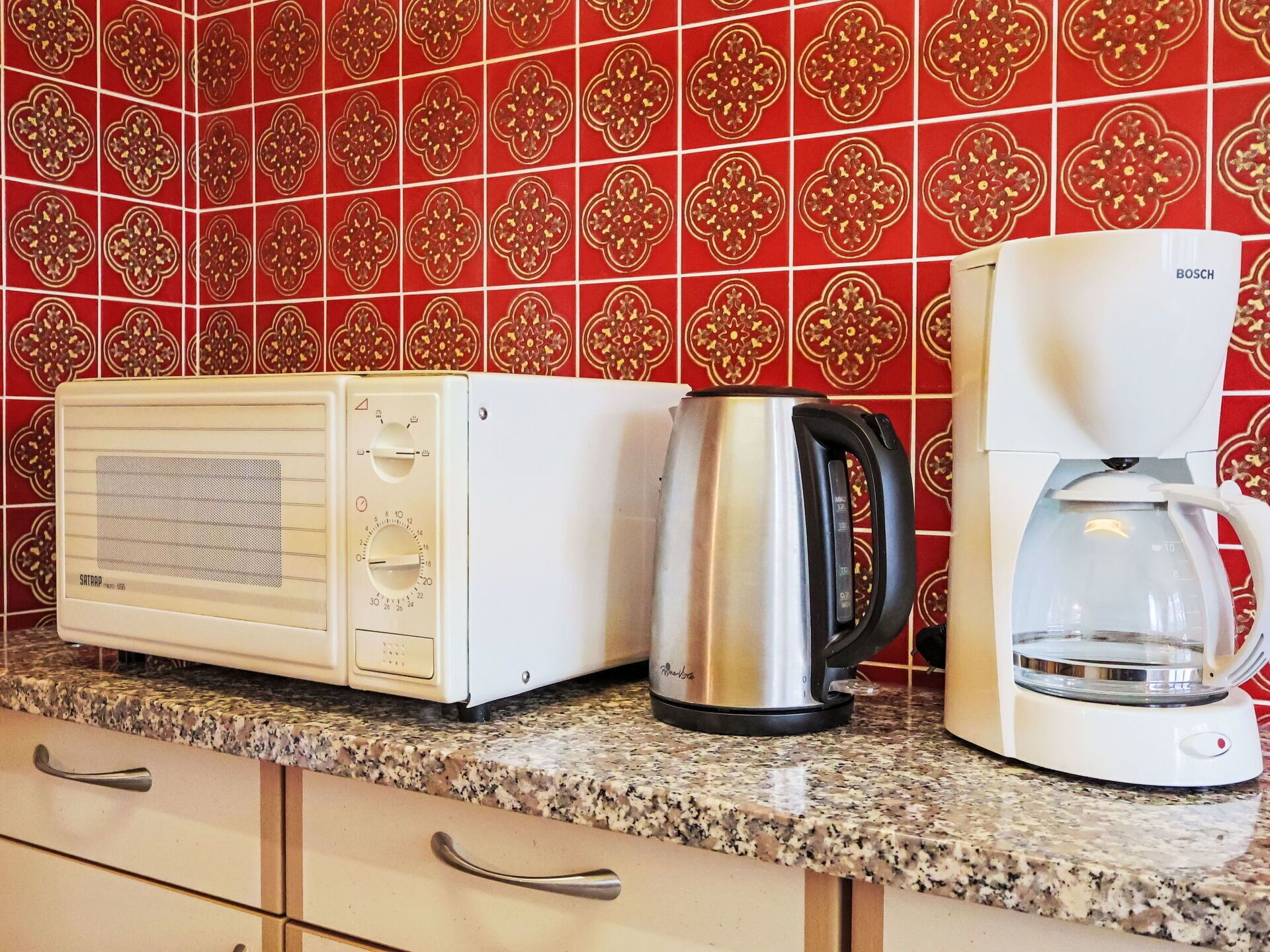 A kitchen with a microwave, a coffee maker, and a kettle on a granite countertop.