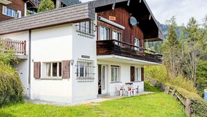 A two-story chalet with a balcony, a small outdoor seating area, and a sign indicating a restaurant.