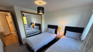 A bedroom with two beds, a mirror, a ceiling light, and a nightstand with a lamp.