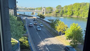 A view of a river with a bridge, cars on the road, and greenery.