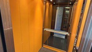 An elevator interior with metallic walls, a glass door, and a metal handrail.