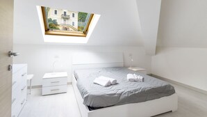 A modern bedroom with a skylight, a bed with a grey quilt, a bedside table, and a white dresser.