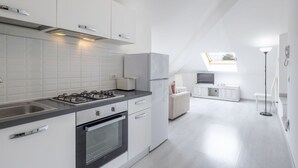 A modern kitchen with white cabinetry, a gas stove, and a built-in oven. There is a small dining area with a white table and a TV.
