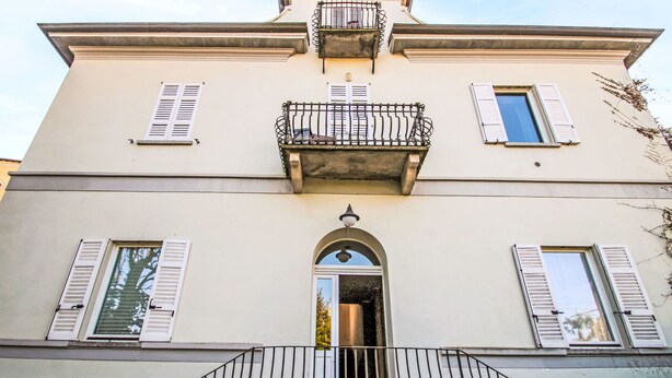 A two-story building with a balcony, shutters, and a central entrance with an archway.